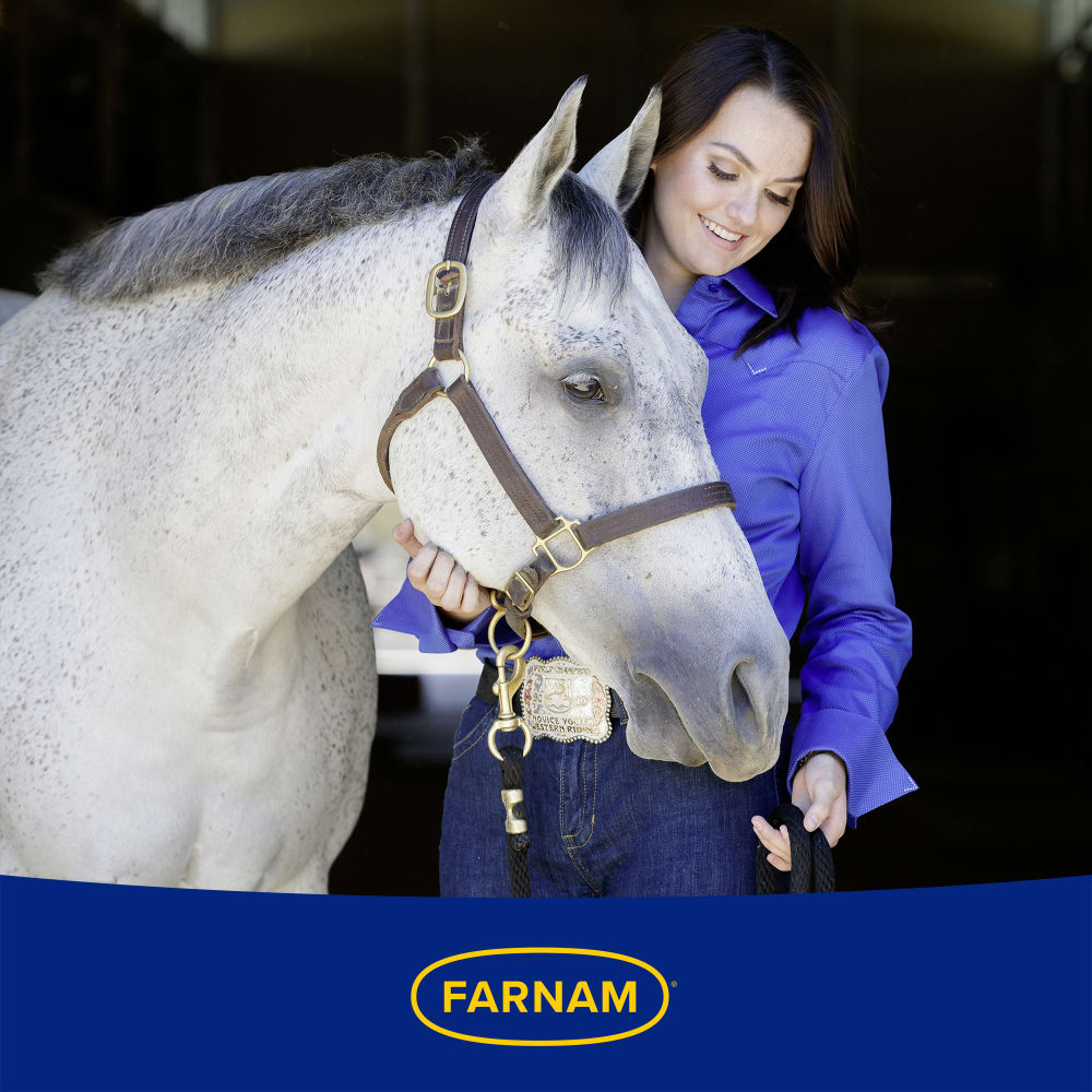 Woman smiling and petting a white horse affectionately. Farnam logo